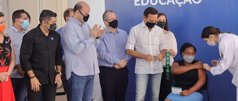 Vacinação de profissionais da educação teve início ontem na Escola Raul Brasil; reuniu o governador, prefeito e secretários. Merendeira foi a 1ª imunizada